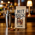 NUTSACK mix packaging on a wooden surface with nuts and a cocktail shaker.